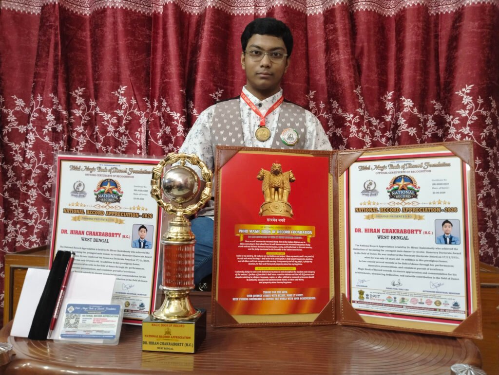 hiran Magic Book of Record Magic Book of Record Young man with glasses sits behind a display of awards medals and certificates on a desk with a red curtain backdrop